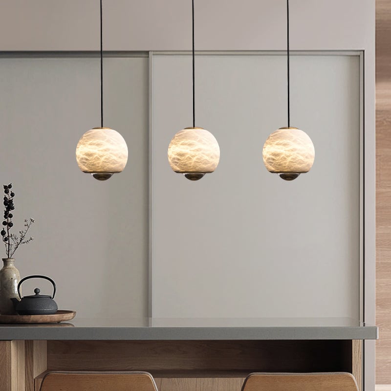 Three glowing alabaster mini pendant lights with natural veining and gold frames hanging over a kitchen counter.
