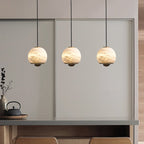 Three glowing alabaster mini pendant lights with natural veining and gold frames hanging over a kitchen counter.