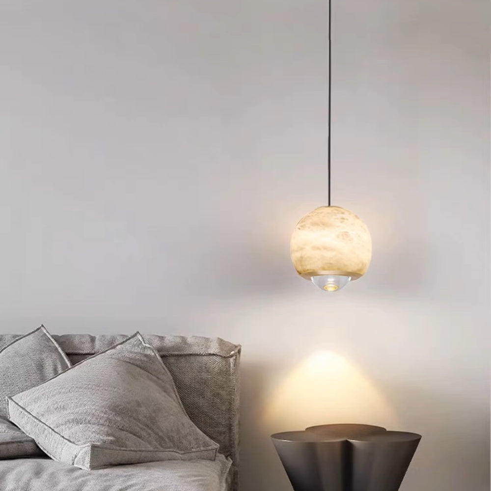 Minimalist alabaster mini pendant light with a gold frame and glowing LED, hanging above a bedside table.