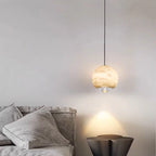 Minimalist alabaster mini pendant light with a gold frame and glowing LED, hanging above a bedside table.