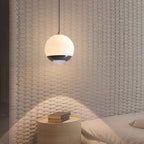 Minimalist 12cm alabaster mini pendant light with a black frame, glowing with integrated LED over a bedside table.