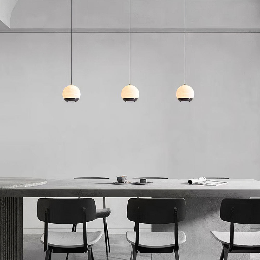 Three minimalist alabaster mini pendant lights with black frames glowing above a modern dining table.