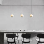 Three minimalist alabaster mini pendant lights with black frames glowing above a modern dining table.