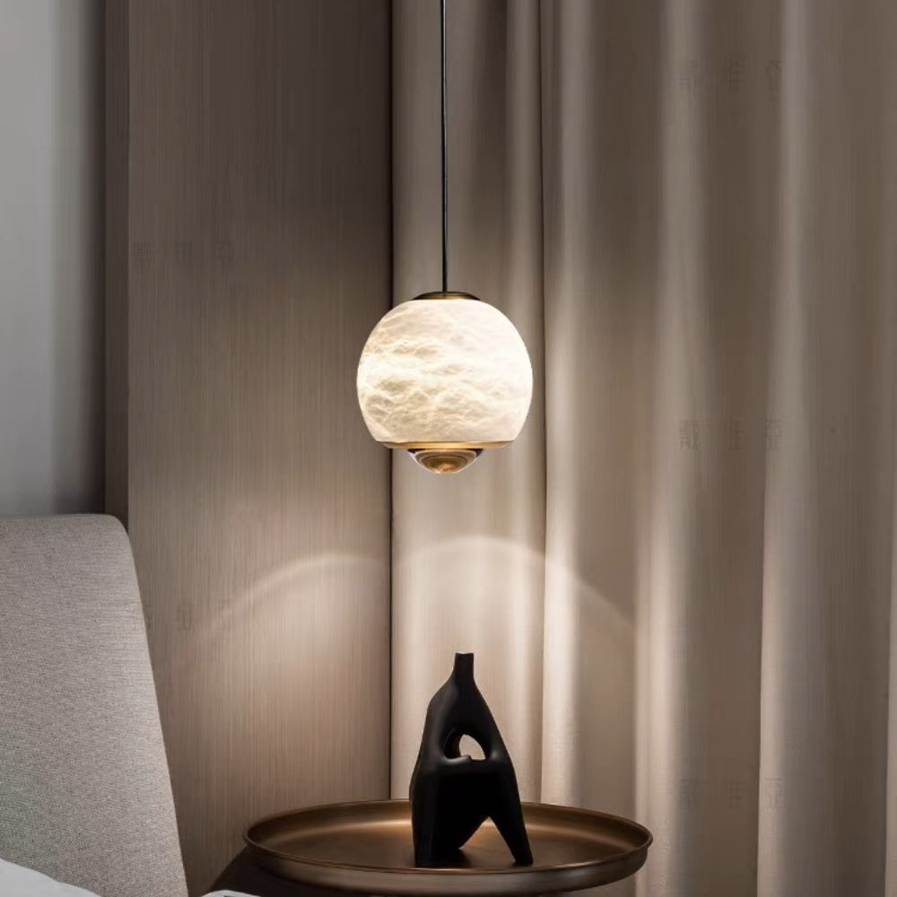 Minimalist alabaster mini pendant light with a gold frame and glowing LED, hanging above a bedside table.