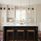 Three sculptural clear glass pendant lights with rippled silhouettes hanging over a kitchen island with dark blue cabinetry.