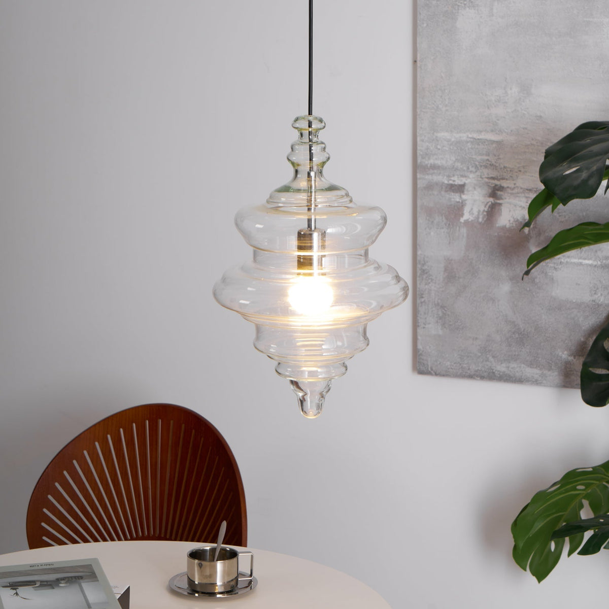 Sculptural clear glass pendant light with a rippled, theatre-inspired silhouette and a warm glowing filament bulb.