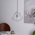 Sculptural clear glass pendant light with a rippled, tiered silhouette hanging above a modern dining table.