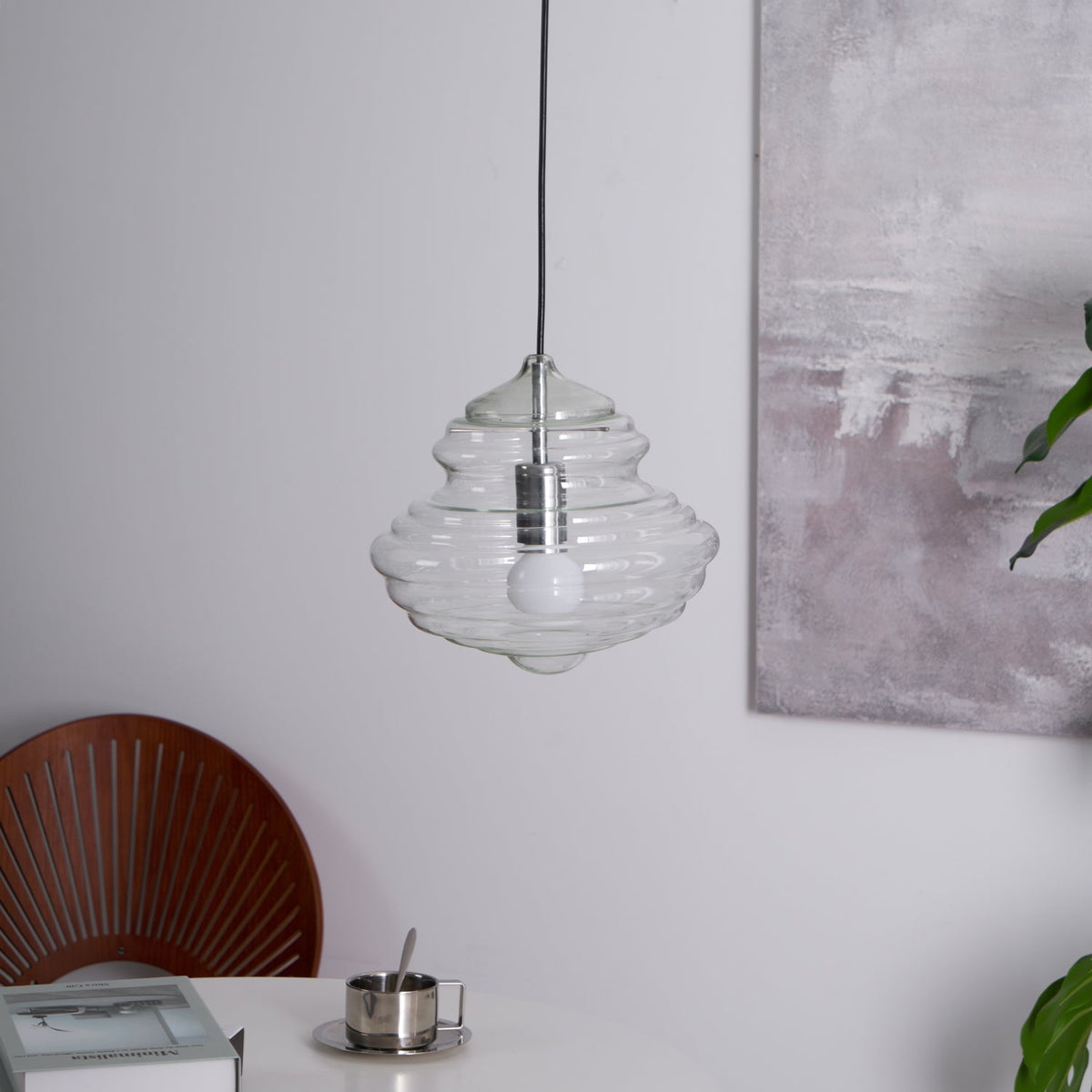 Sculptural clear glass pendant light with a rippled, tiered silhouette hanging above a modern dining table.