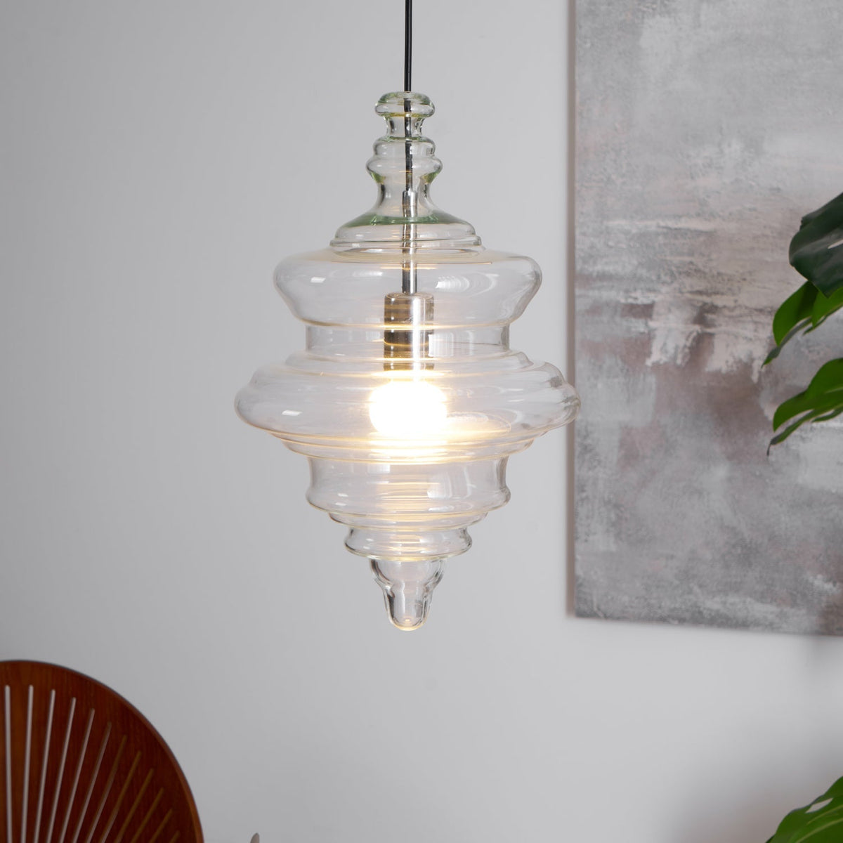 Sculptural clear glass pendant light with a rippled, theatre-inspired silhouette and a warm glowing filament bulb.