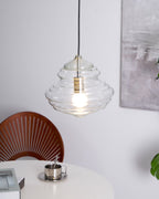 Sculptural clear glass pendant light with a rippled, tiered design and a warm glowing filament bulb.