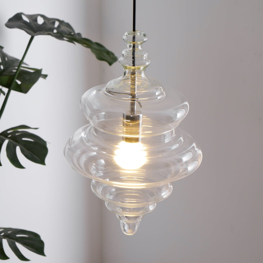 Sculptural clear glass pendant light with a rippled, theatre-inspired silhouette and a warm glowing filament bulb.