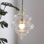 Sculptural clear glass pendant light with a rippled, theatre-inspired silhouette and a warm glowing filament bulb.