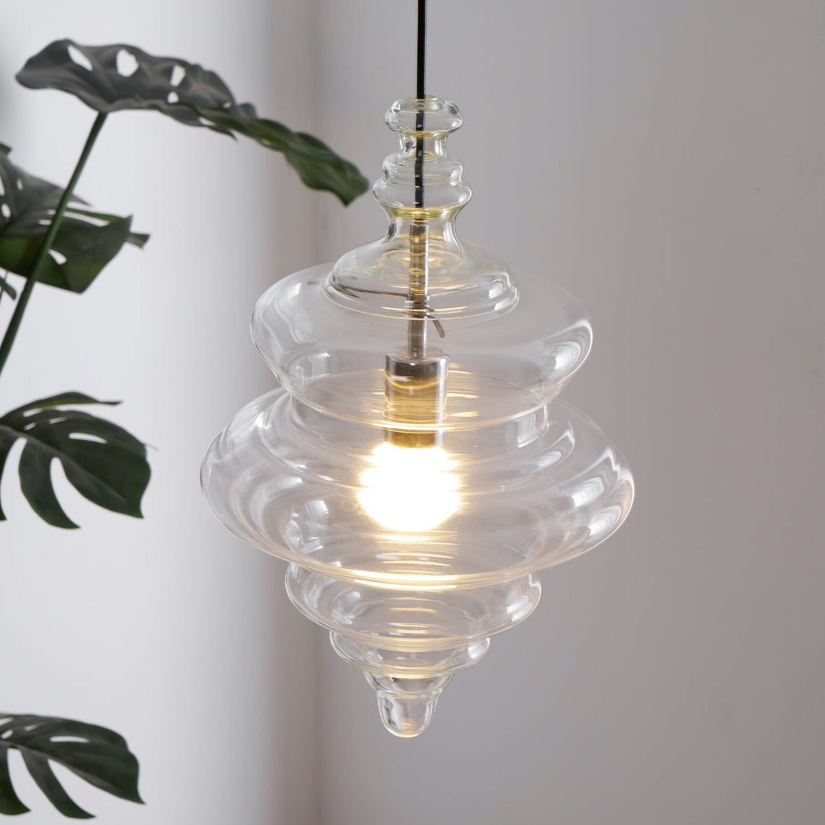 Sculptural clear glass pendant light with a rippled, theatre-inspired silhouette and a warm glowing filament bulb.