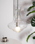 Sculptural clear glass pendant light with a rippled silhouette and warm filament bulb, hanging in a modern interior.