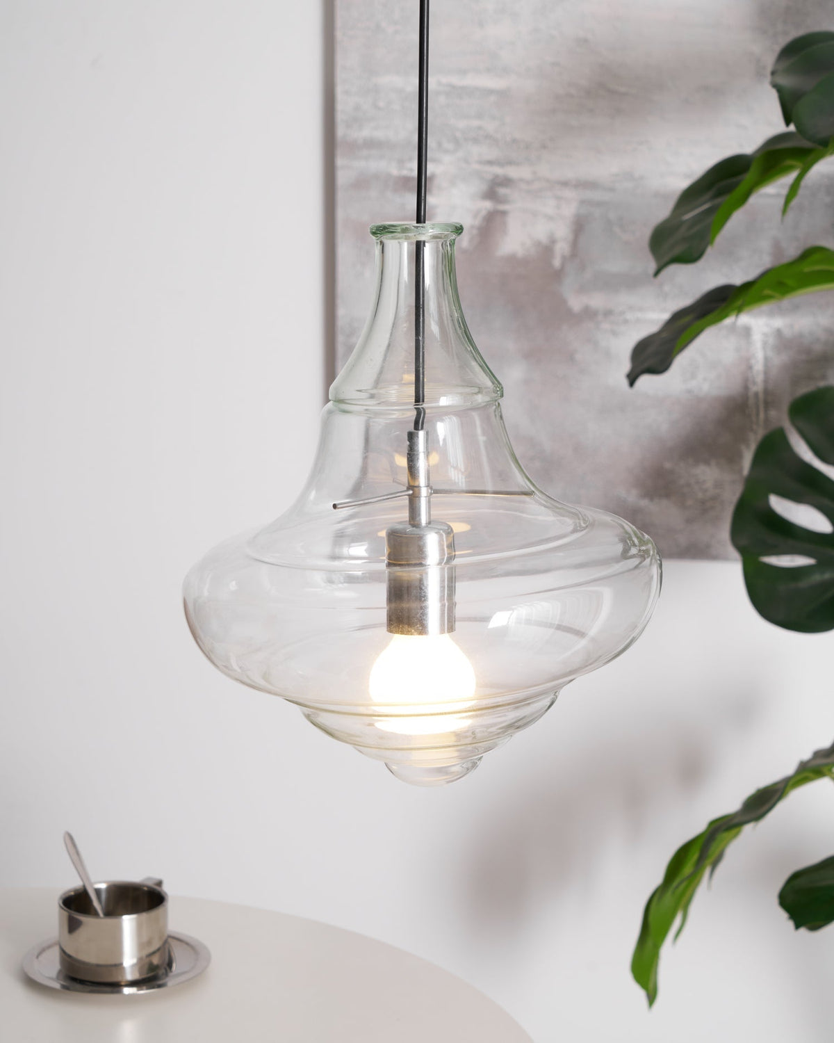 Sculptural clear glass pendant light with a rippled silhouette and warm filament bulb, hanging in a modern interior.