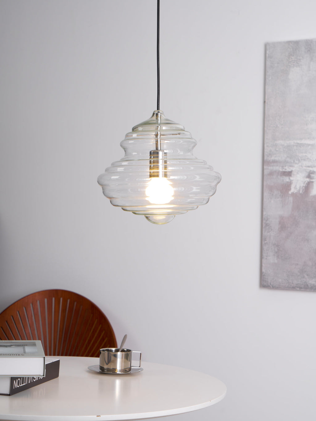 Sculptural clear glass pendant light with rippled texture and warm filament bulb, hanging above a dining table.