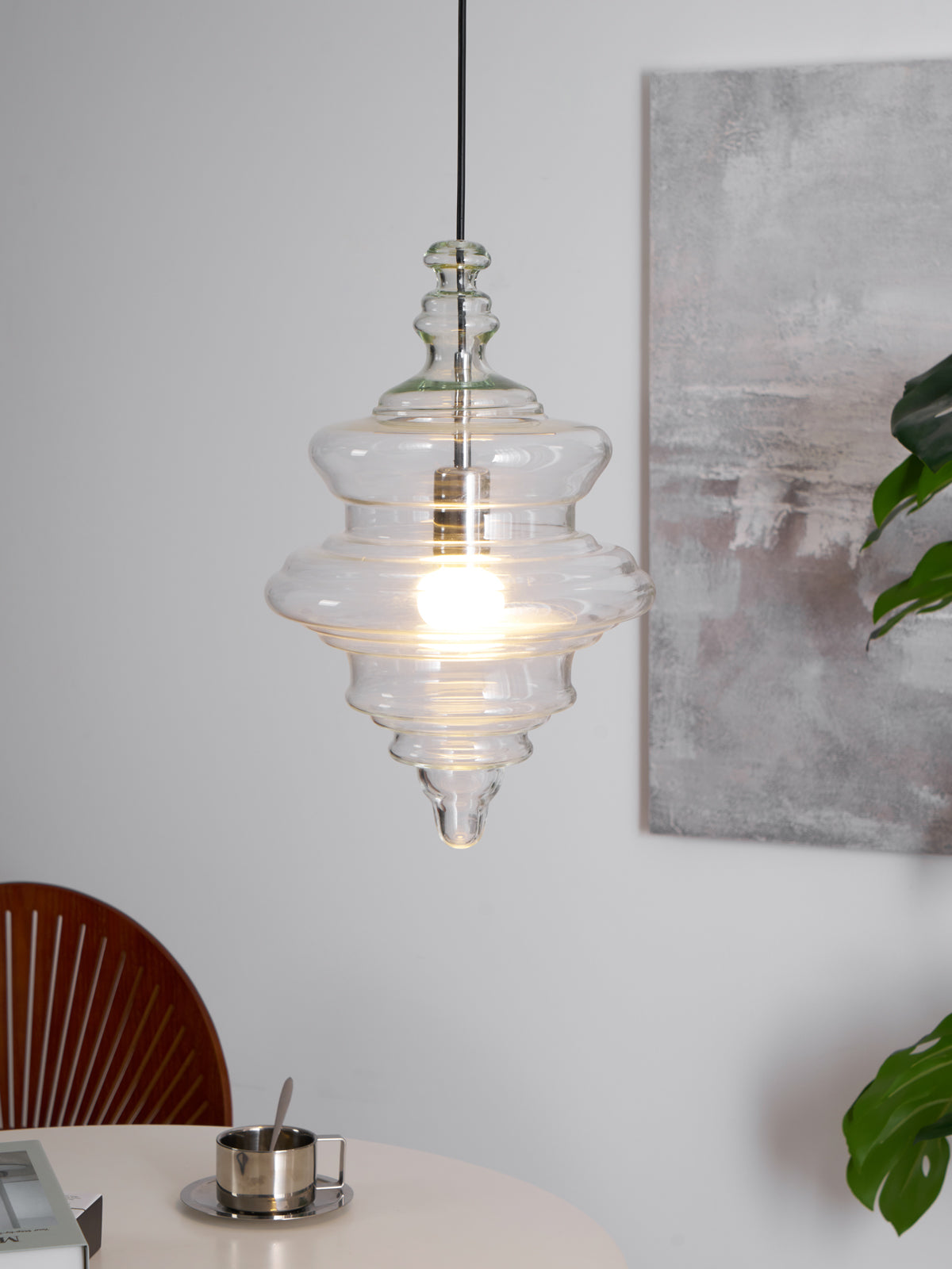 Sculptural clear glass pendant light with a rippled, theatre-inspired silhouette and warm glowing filament bulb.