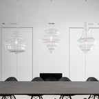 Three sculptural clear glass pendant lights with rippled silhouettes hanging above a modern dining table.