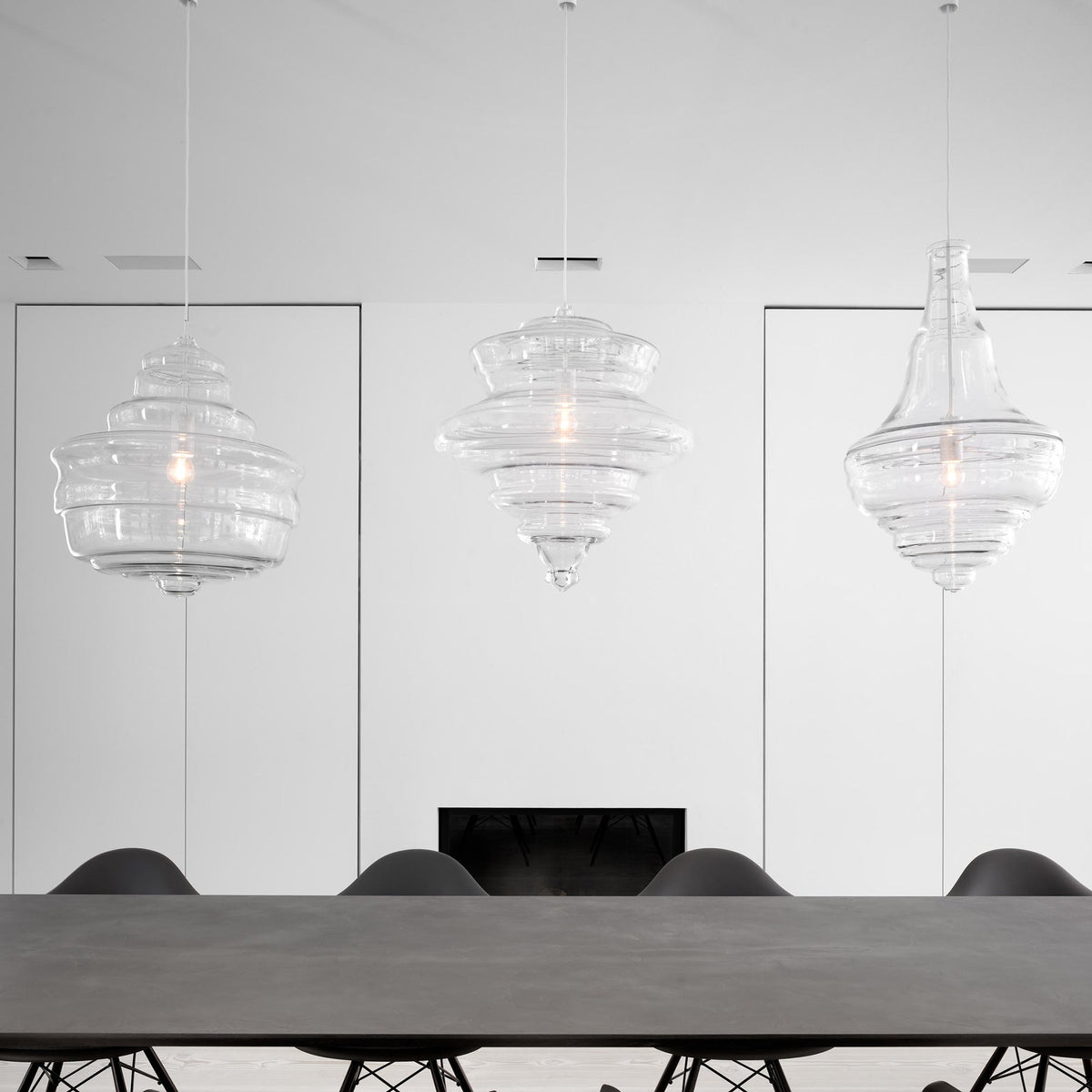Three sculptural clear glass pendant lights with rippled silhouettes hanging above a modern dining table.