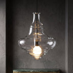 Sculptural clear glass pendant light with a rippled silhouette and warm filament bulb against a dark background.