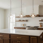 Three sculptural clear glass pendant lights hanging over a modern kitchen island with warm filament bulbs.