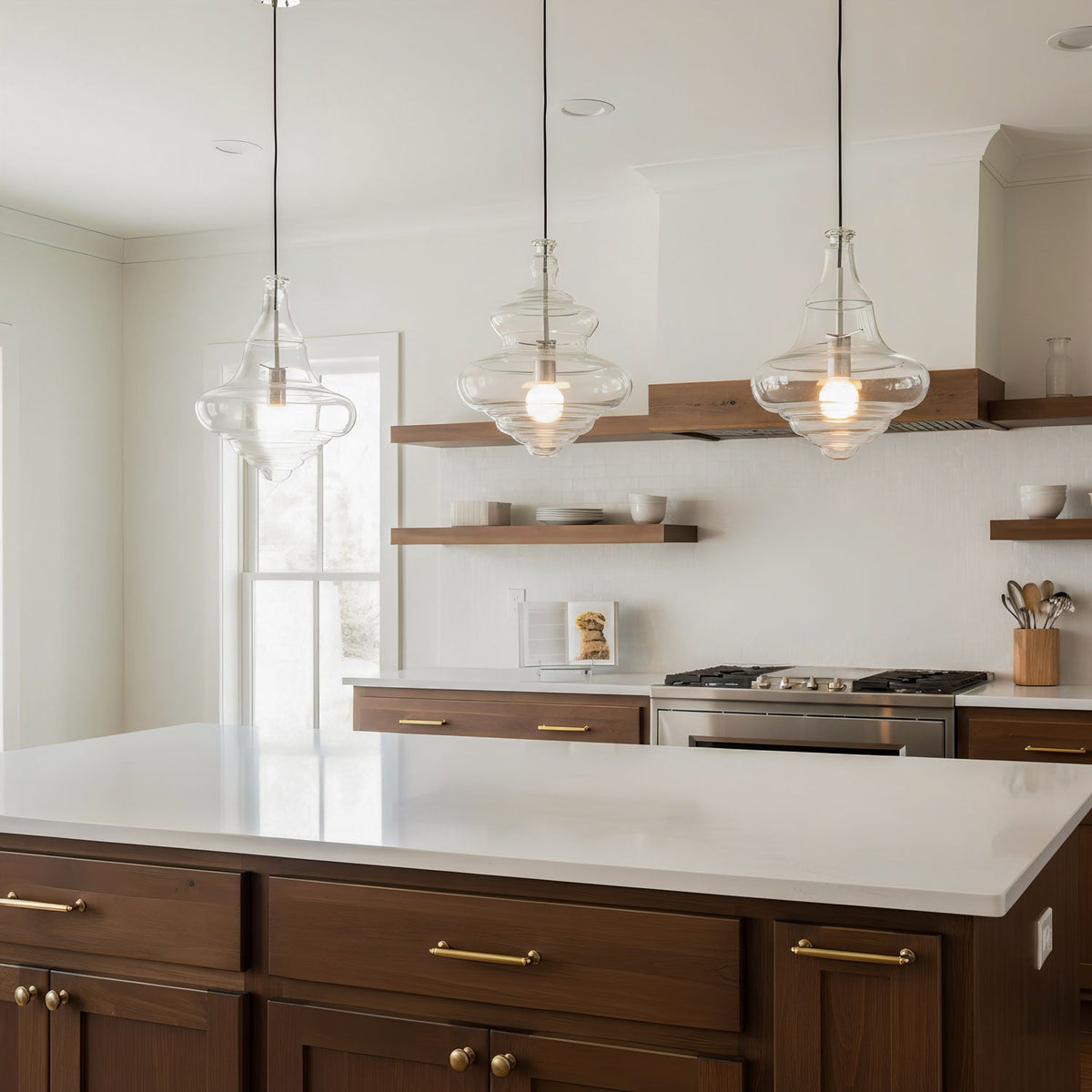 Three sculptural clear glass pendant lights hanging over a modern kitchen island with warm filament bulbs.