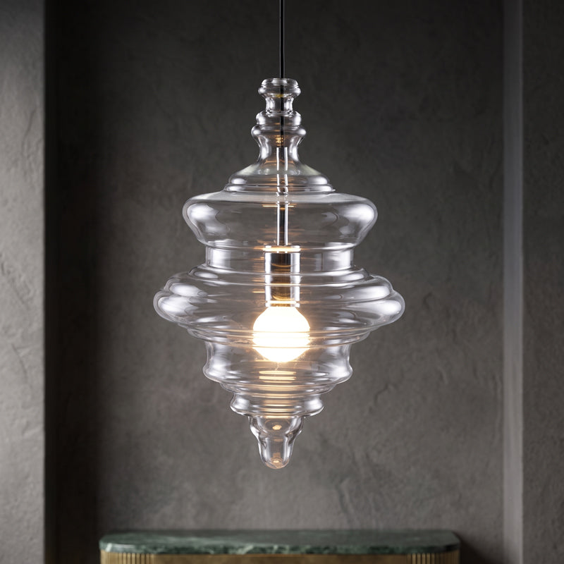 Sculptural clear glass pendant light with a rippled, theatre-inspired silhouette and a warm glowing filament bulb.