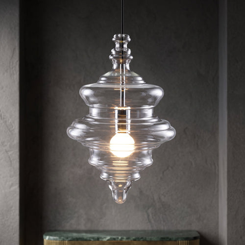 Sculptural clear glass pendant light with a rippled, theatre-inspired silhouette and a warm glowing filament bulb.
