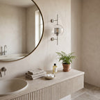 Clear Glass Wall Light – Silver / A in a spa-like bathroom beside a large round mirror and stone vanity