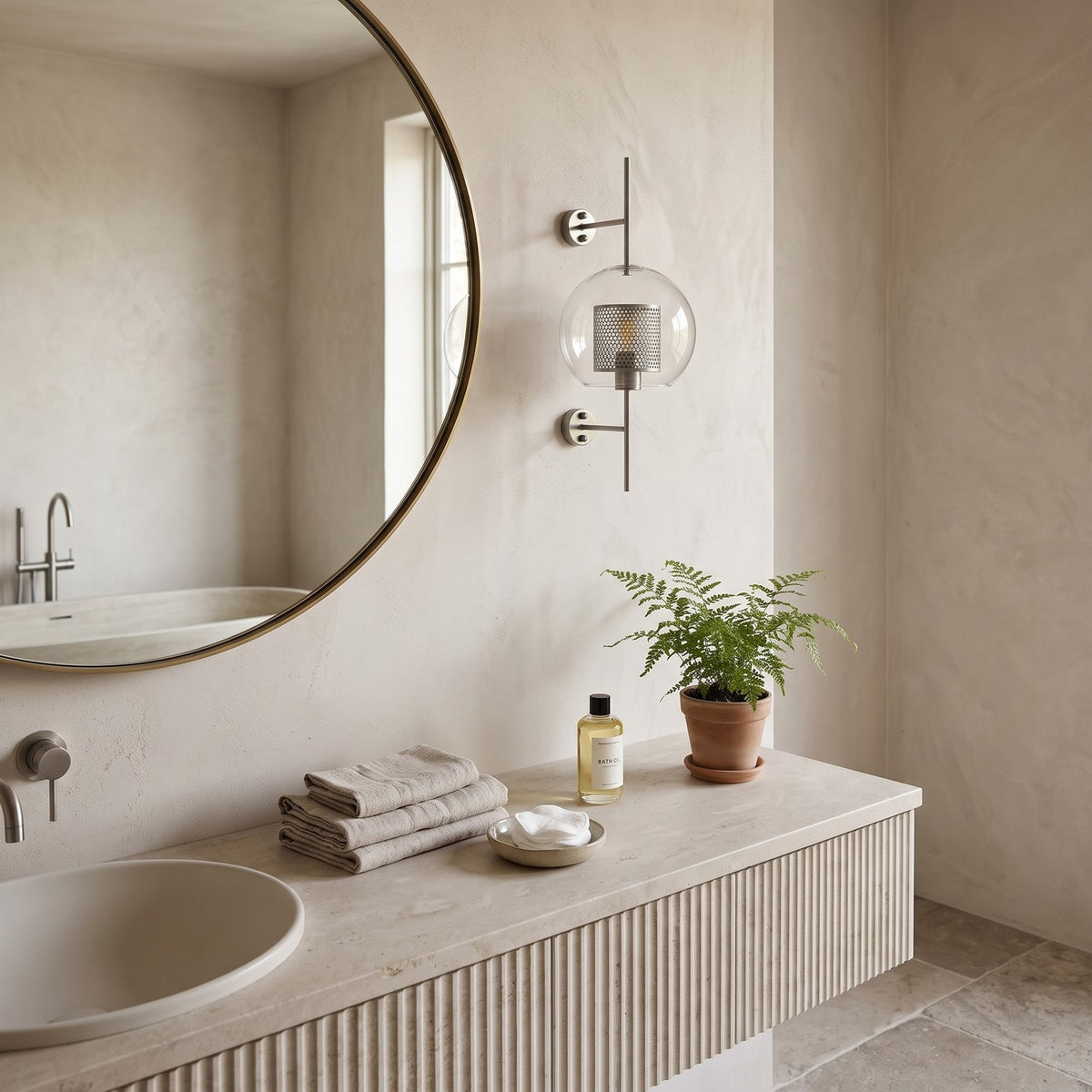 Clear Glass Wall Light – Silver / A in a spa-like bathroom beside a large round mirror and stone vanity