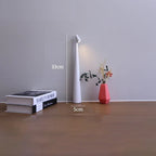 Slim white cordless LED table lamp, 33cm tall with a minimalist design, placed on a wooden surface next to books and a vase.