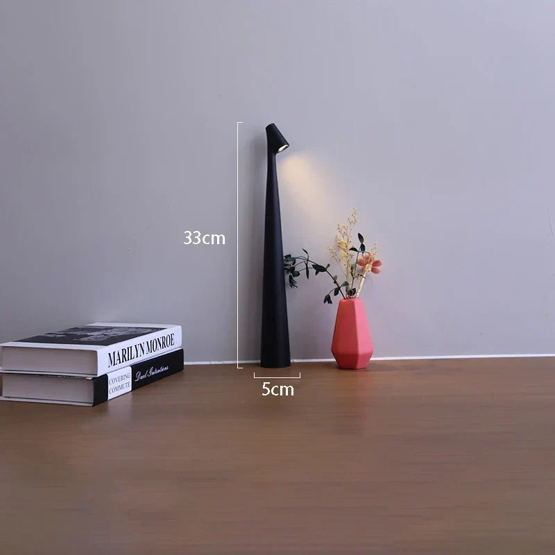 Slim black cordless LED table lamp, 33cm tall with a 5cm base, shown on a desk next to books and a small vase.