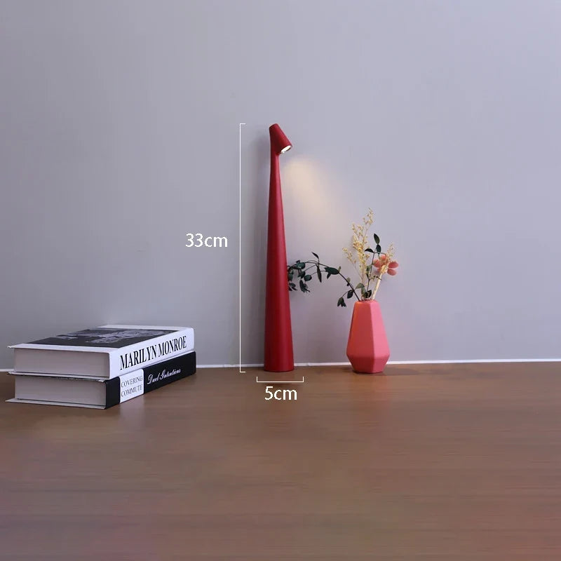 Slim red cordless LED table lamp, 33cm tall with a minimalist design, placed on a surface next to books and a small vase.