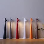 Six slim, minimalist cordless LED table lamps in black, grey, red, white, orange, and brown standing on a wooden surface.