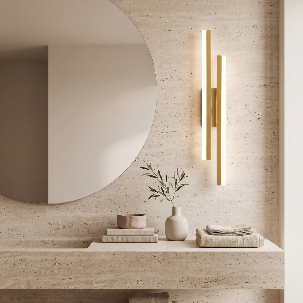 Geometric LED Wall Light – Gold / Left in a spa-like bathroom beside a large round mirror and stone vanity