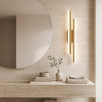 Geometric LED Wall Light – Gold / Left in a spa-like bathroom beside a large round mirror and stone vanity