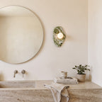 Green Marble Wall Light – Model A in a spa-like bathroom beside a large round mirror and stone vanity