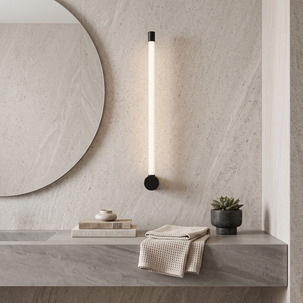 LED Tube Wall Light – Black-end in a spa-like bathroom beside a large round mirror and stone vanity