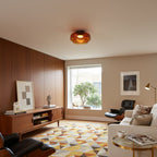 Retro layered orange glass ceiling light fixture in a mid-century modern living room with wood paneling.
