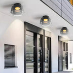 Three smoky grey layered glass ceiling lights with warm glowing bulbs mounted on a modern white exterior ceiling.