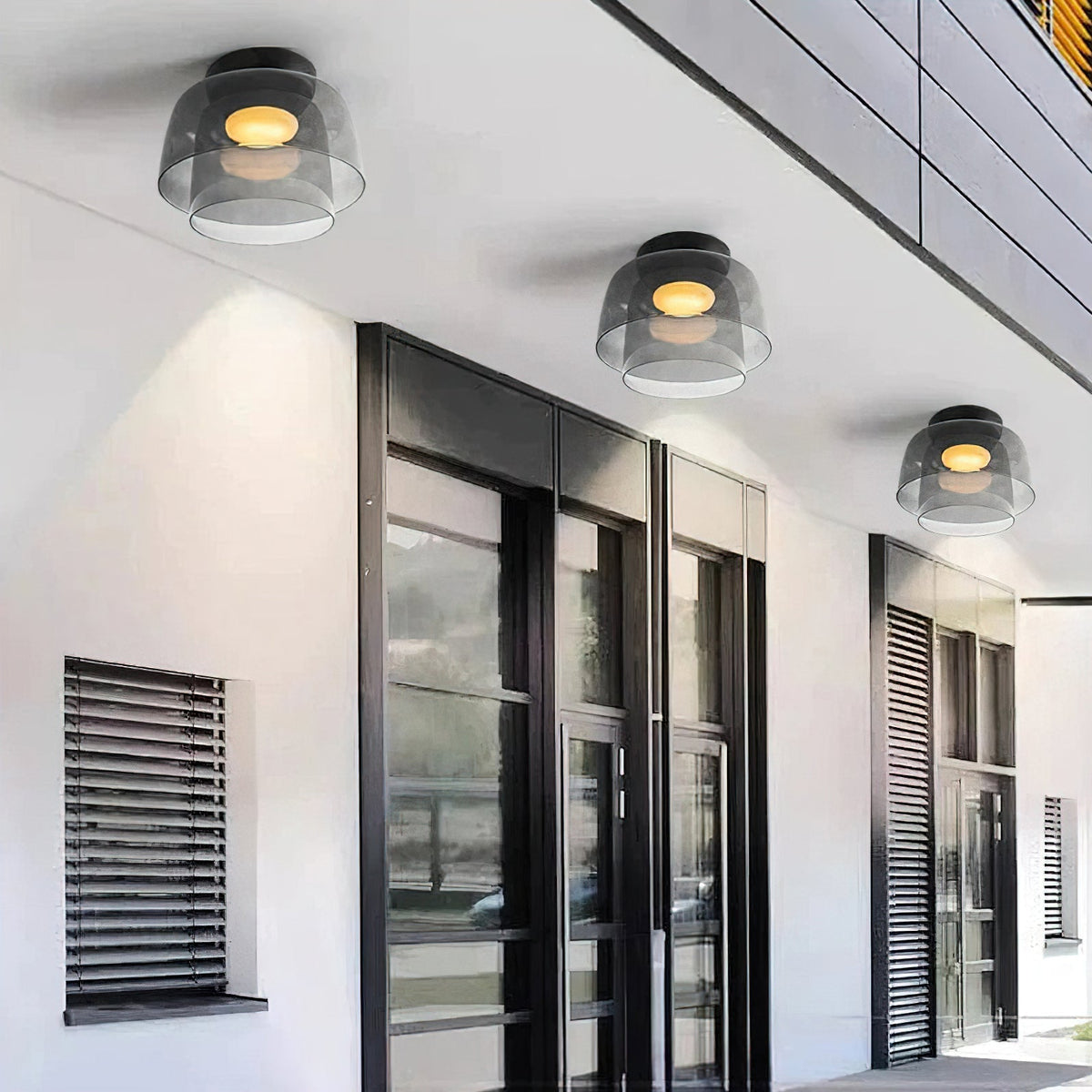 Three smoky grey layered glass ceiling lights with warm glowing bulbs mounted on a modern white exterior ceiling.