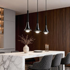 Three modern chrome and black teardrop LED pendant lights hanging over a marble dining table.