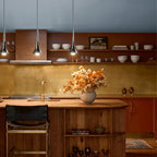 Three modern chrome teardrop pendant lights hanging over a wooden kitchen island with warm LED illumination.