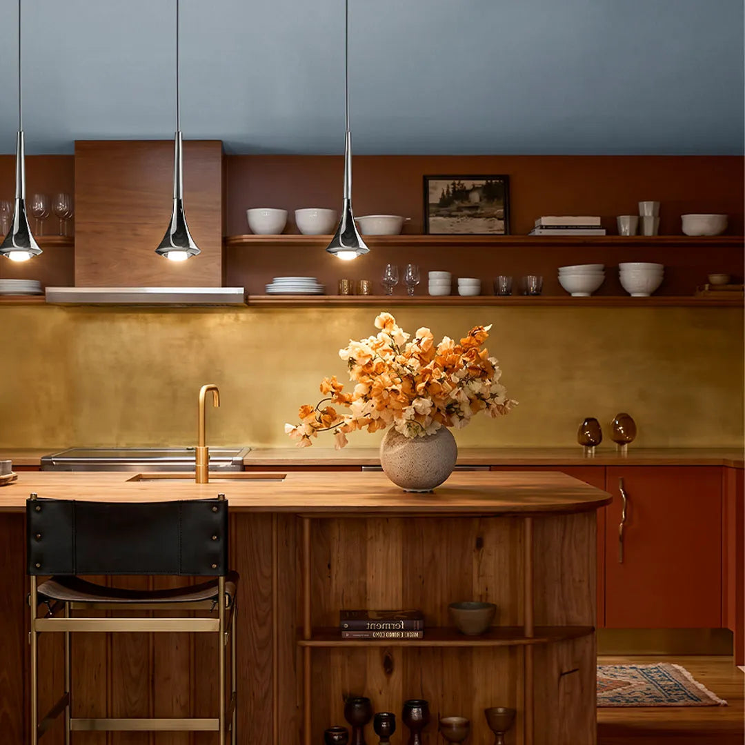 Three modern chrome teardrop pendant lights hanging over a wooden kitchen island with warm LED illumination.