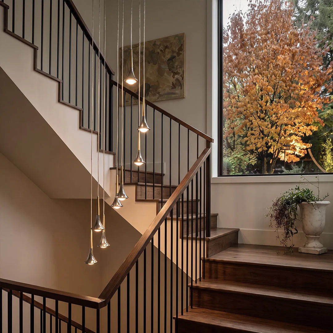 Modern chrome teardrop LED pendant lights hanging in a staggered cluster above a wooden staircase.