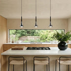 Three chrome teardrop LED pendant lights hanging over a modern kitchen island with a view of a garden.