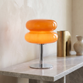 Retro orange glass table lamp with a rounded, 70s space-age design on a polished chrome base sitting on a marble table.