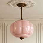Vintage semi-flush ceiling light with a sculpted soft pink glass shade and antique brass hardware on a decorative ceiling.