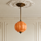 Vintage semi-flush ceiling light with a round, peach-colored sculpted glass shade and antique brass hardware.