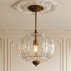 Vintage semi-flush ceiling light with a clear sculpted glass shade and antique brass hardware on a decorative ceiling rose.